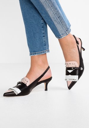 Zwart-roze slingback kitten heels met zilverkleurige studs, gedragen met cropped blauwe jeans op een witte vloer.