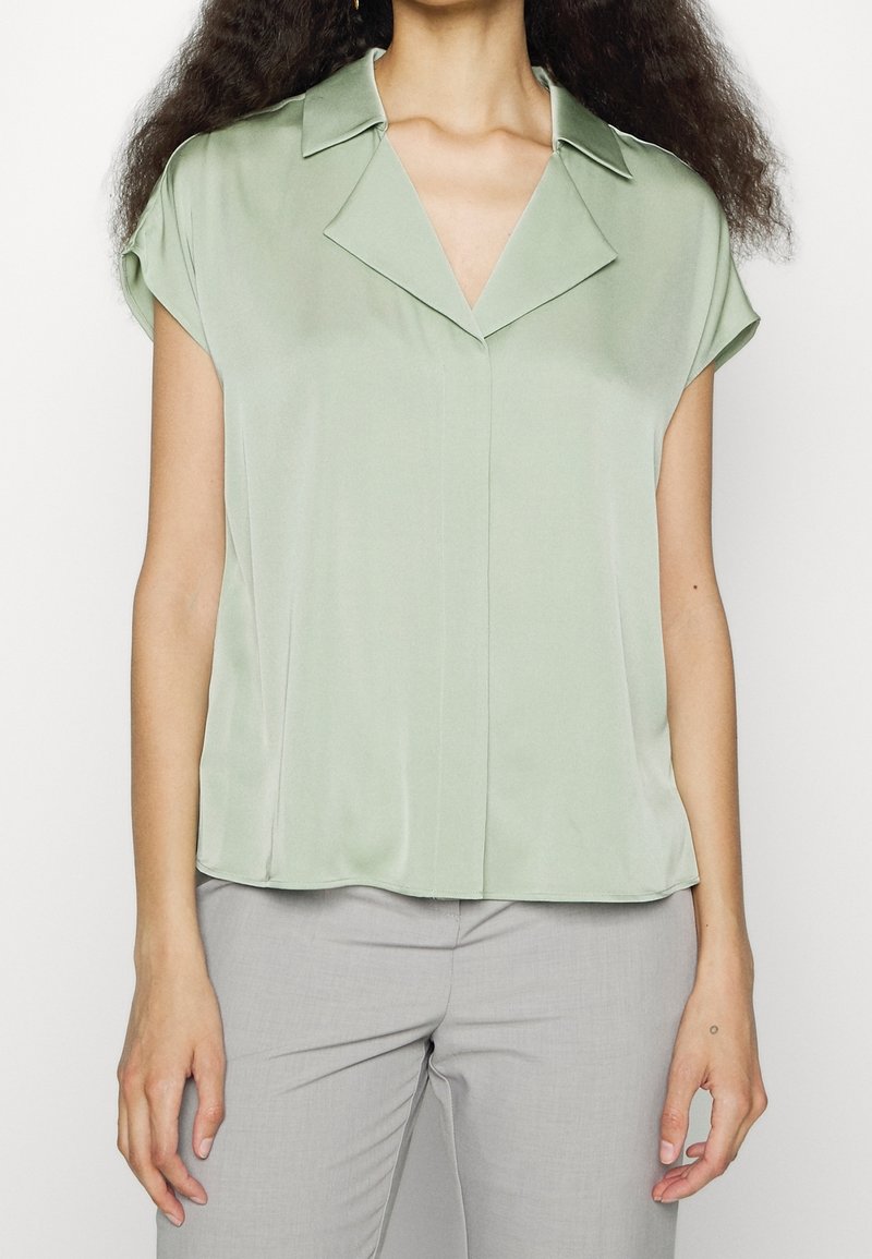 Satinblus i olivgrön med krage och korta ärmar, med knäppning framtill och avslappnad passform. Slät textur som faller mjukt.