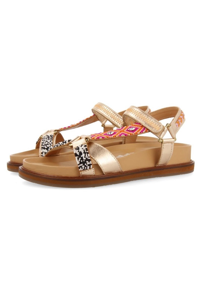 Guld sandaler med en flettet rem, flerfarvet perledesign og flad sål. Har justerbare ankelremme og et struktureret mønster.