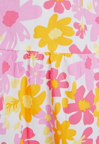 Tecido de algodão floral com grandes flores rosas e amarelas sobre um fundo branco. Detalhes franzidos na cintura com textura suave.