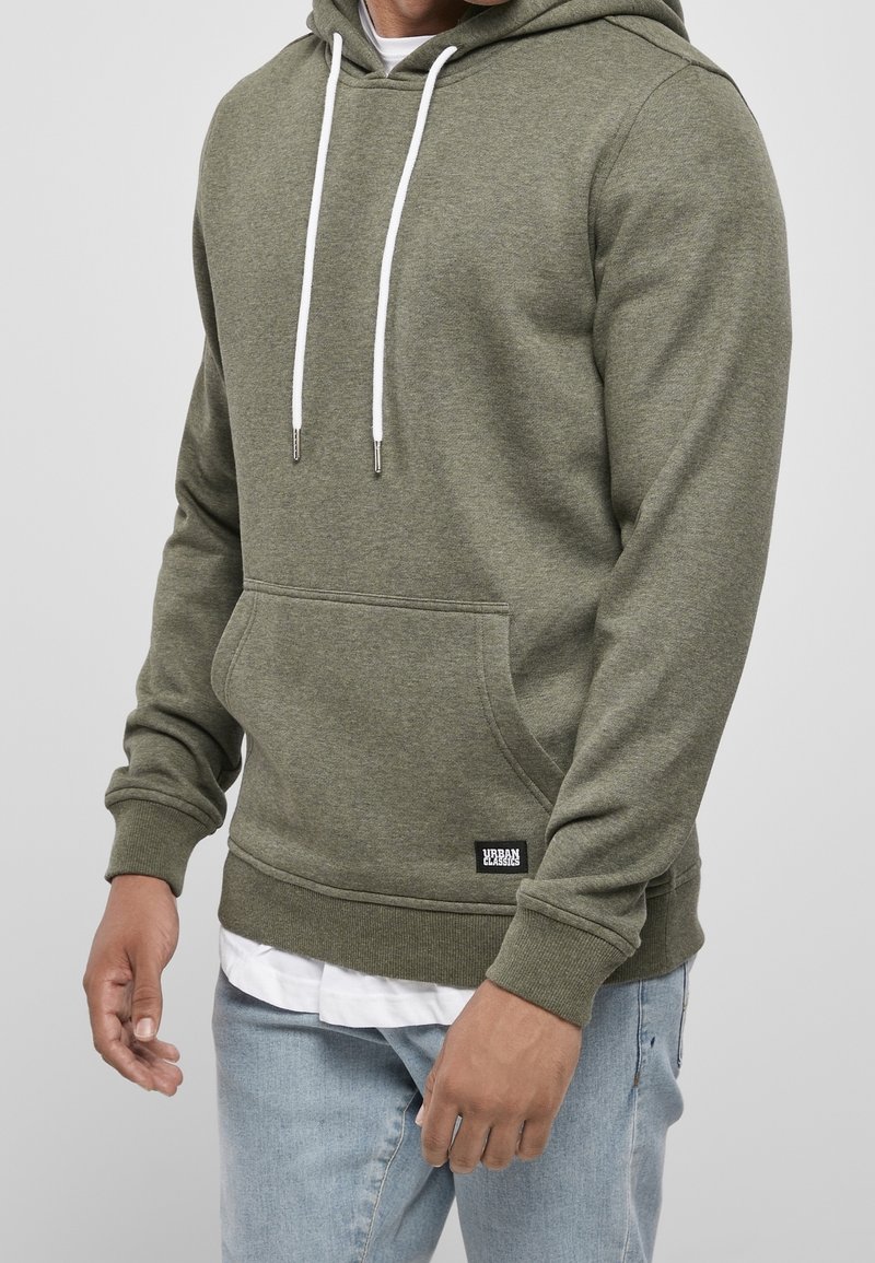 Olivenfarbener Kapuzenpullover aus weichem Material, mit einer Kängurutasche, weißen Kordeln, gerippten Bündchen und einem kleinen Markenpatch am Saum.
