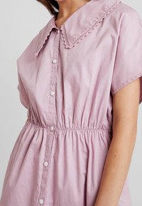 Abito di cotone rosa con un ampio colletto scallop, maniche corte, vita elastica e chiusura a bottoni sul davanti; presenta una finitura morbida e testurizzata.