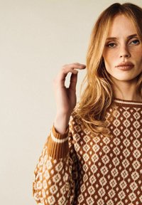 Brun mönstrad tröja med diamantmönster, ribbade muddar och rundad nacke. Den mjuka texturen och de varma färgtonerna förstärker designen.