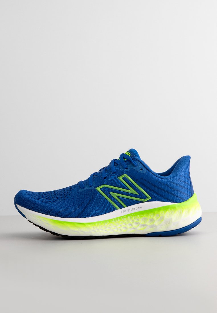 Zapatilla deportiva azul con una parte superior texturizada, detalles en verde y una suela acolchada que presenta una sección translúcida en verde lima.