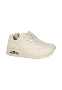 Zapatillas beige con material perforado y lengüeta acolchada, que presentan una almohadilla de aire visible en la suela y una suela exterior de goma texturizada.