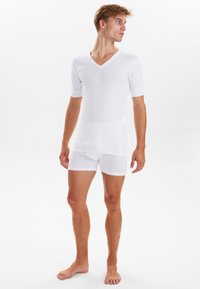Hvid V-hals kortærmet skjorte parret med hvide boxer shorts, begge lavet af glat, let stof, tætsiddende design med enkel styling.