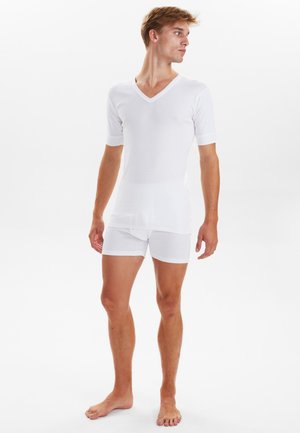 Hvid V-hals kortærmet skjorte parret med hvide boxer shorts, begge lavet af glat, let stof, tætsiddende design med enkel styling.