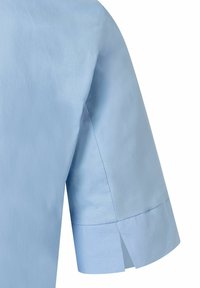 Hellblaues Kurzarmhemd mit glatter Textur, klassischem Kragen und Seitenschlitzen am Saum für zusätzlichen Bewegungskomfort.