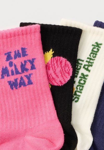 Quatre chaussettes colorées avec des textes et motifs tricotés ; la rose affiche "THE MILKY WAY", la noire a une planète rose, la blanche dit "STEPX AHEAD", la marine est partiellement visible.