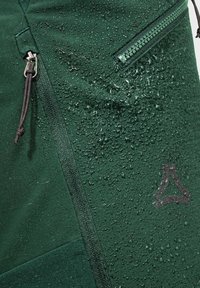 Grüne wasserdichte Jacke mit einer strukturierten Oberfläche und sichtbaren Wassertropfen, mit Reißverschlusstaschen und einem Logo in der unteren rechten Ecke.
