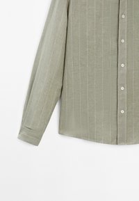 Camicia a maniche lunghe verde chiaro realizzata in tessuto testurizzato, con strisce bianche verticali, apertura con bottoni sul davanti e dettagli ai polsini con bottoni.