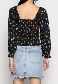 Blouse florale noire avec de longues manches bouffantes, dos froncé et décolleté carré, associée à une jupe en denim délavé bleu clair.