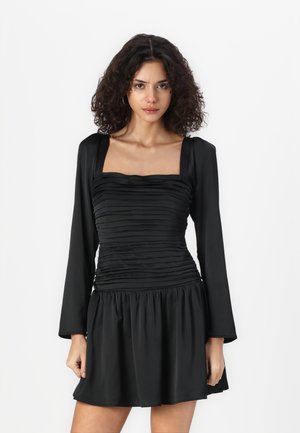 Robe noire avec un décolleté carré, des manches longues et une texture froncée au niveau du buste. Jupe évasée avec une finition lisse.