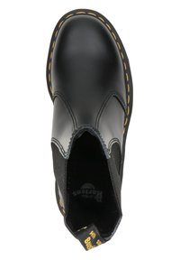 Bota negra de cuero tipo slip-on con paneles elásticos en los laterales y costuras amarillas alrededor de la suela, vista desde arriba.