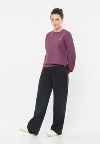 Felpa bordeaux con scollatura rotonda e dettagli ricamati, abbinata a jeans neri a vita alta e a gamba larga, con scarpe di colore chiaro.