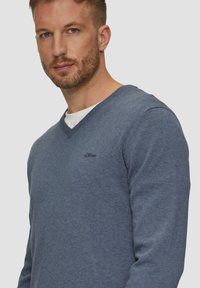 Dunkelblauer V-Ausschnitt-Pullover aus Stoff, mit einem gerippten Kragen und Bündchen, versehen mit einem kleinen schwarzen "s.Oliver"-Logo auf der linken Brust.