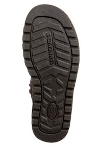 Suela de zapato de goma negra con un patrón de textura, con el nombre de la marca "Skechers" embossado en el centro. Diseño duradero y flexible.