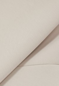 Tessuto beige chiaro con una texture liscia e un sottile motivo fine, piegato per mostrare più strati e una leggera lucentezza.