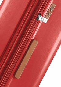Valigia rigida rossa con doppie cerniere, lucchetto TSA e finitura texturizzata. Presenta un accento marrone sul lato per una migliore presa.