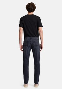 Dunkelblaue Jeans mit geradem Bein, Gesäßtaschen mit Nähakzenten, getragen mit einem schlichten schwarzen T-Shirt.