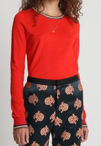 Suéter rojo de manga larga con un cuello a rayas en contraste, combinado con pantalones negros con estampado de motivos animales en varios colores.