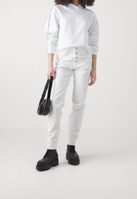 Bílá mikina s volnými rameny, kombinovaná s bílými džíny s vysokým pasem a předními knoflíky. Černé platformové boty a malá černá kabelka.