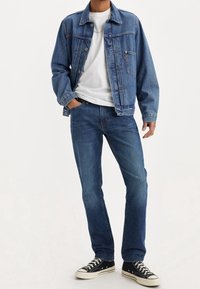 Jeansjacka och jeans i blått, med klassisk passform, knappstängning, framfickor, kombinerat med en vit T-shirt och svarta sneakers.