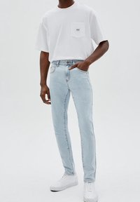 Vit bomull T-shirt med bröstficka, tillsammans med ljusblå tajta jeans. Vita sneakers fulländar outfiten. Enkelt mönster och färgschema.