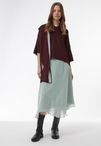 Bordeaux gebreide top met brede mouwen, gecombineerd met een vloeiende mintgroene asymmetrische rok, aangevuld met zwarte kniehoge laarzen.