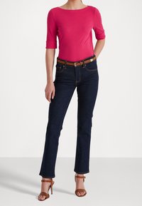 Rosa åtsittande topp med trekvartsärmar, kombinerad med mörkblå jeans med utställda ben och bruna strappy klacksandaler. Brun bälte som accent.