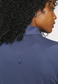 Ναυτικό αθλητικό μπλουζάκι με υφή στον γιακά και V-σχηματική διακόσμηση στην πλάτη. Διαθέτει απαλό, ύφασμα που απομακρύνει την υγρασία.