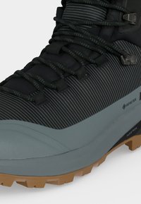 Κοντινή λήψη μαύρου και γκρι ορειβατικού μπότες με ύφασμα Gore-Tex, κορδόνια με σχέδιο και καφέ ανθεκτική σόλα σχεδιασμένη για υπαίθρια εδάφη.