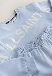 Šviesiai mėlynas megztinis ir derančios kelnės iš minkštos medžiagos. Megztinis puošiamas dideliais baltais užrašais. Kelnėse yra surinktasis juosmuo.