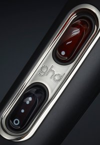 Gros plan sur un appareil électronique noir et argenté avec deux boutons ovales et un logo "ghd" en pointillés en relief sur une plaque métallique.