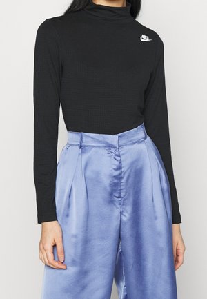 Personne portant un haut col roulé noir à manches longues Nike et un pantalon satiné bleu clair brillant taille haute.