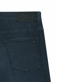 Dark blue denim jeans with a smooth texture, featuring a leather BOSS logo patch at the waistband and a single back pocket detail.