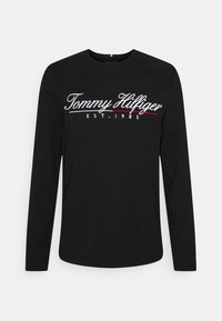 T-shirt a maniche lunghe nera in cotone, con logo ricamato "Tommy Hilfiger" in bianco e rosso e "EST. 1985" sottostante.