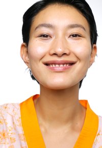 Ljusrosa blommig blus med en orange krage. Slät hud och kort mörkt hår, som visar ett avslappnat leende och naturlig sminkning.