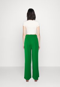 Pantalon vert à jambes larges avec une taille élastique. Confectionné dans un tissu lisse et léger. Vue de dos, porté avec un haut ajusté de couleur claire.