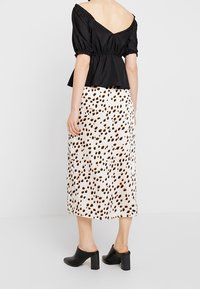 Černý top bez ramínek s peplum střihem a nabíranými rukávy; sukně střední délky krémové barvy s abstraktními hnědými skvrnami; doplněno černými muly s robustním podpatkem.