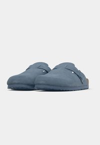 Μπλε σουέτ ξύστρες με στρογγυλεμένη μύτη, πλευρικούς ιμάντες και υφασμένα λαστιχένια πέλματα. Λιτή επιφάνεια με φελλό στην εσωτερική σόλα για άνεση.