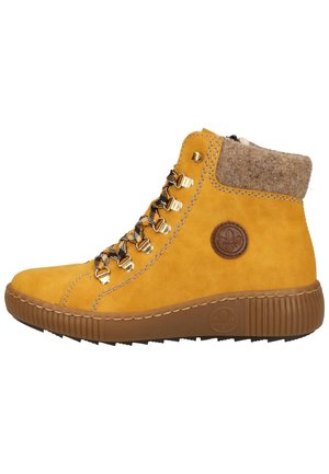 Bottes à la cheville en daim jaune avec un col en laine, semelle en caoutchouc marron, accessoires dorés et lacets noir et blanc. Logo en relief sur le côté.