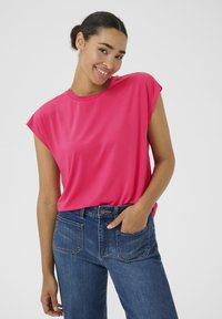 Rosa Kurzarmoberteil aus glattem Stoff, mit rundem Halsausschnitt und lockerer Passform, kombiniert mit blauen Jeans.
