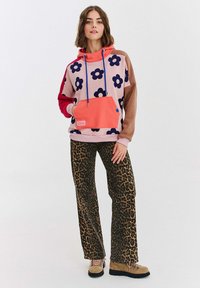 Veľká mikina s kvetinovým vzorom v ružovej, modrej a červenej farbe, so klokankou. Spárovaná s hnedými nohavicami s leopardím vzorom a širokými nohavicami.