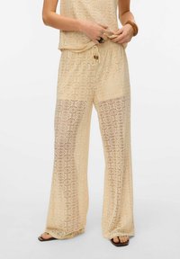 Lace twee-delige outfit in lichtbeige met cirkelpatronen, bestaande uit losse broek en een bijpassend topje. Koordsluiting in de taille en doorzichtige textuur.