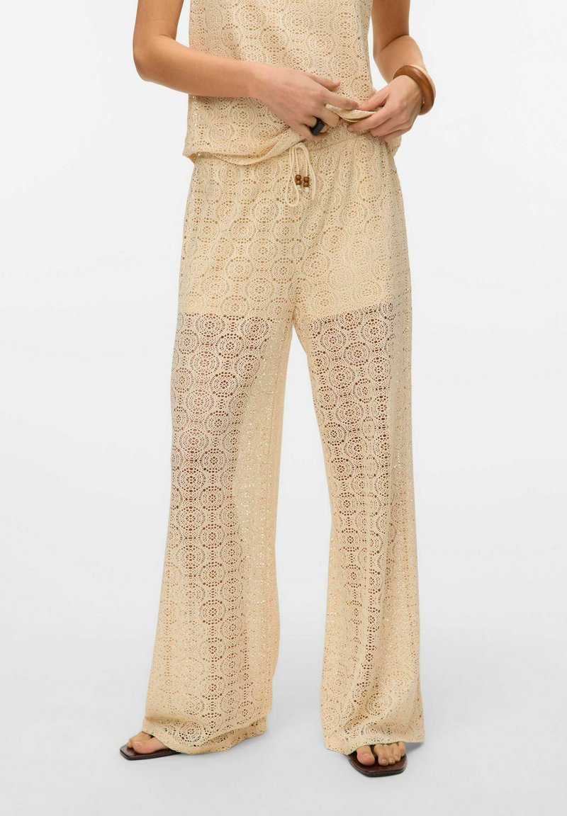 Lace twee-delige outfit in lichtbeige met cirkelpatronen, bestaande uit losse broek en een bijpassend topje. Koordsluiting in de taille en doorzichtige textuur.