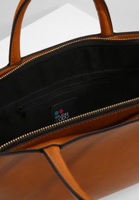 Sac à main en cuir marron avec doublure en tissu noir, doté d'une fermeture éclair et d'une poche intérieure. Étiquette du logo visible à l'intérieur.