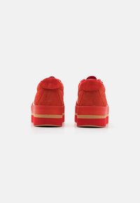 Baskets plateformes en suède rouge avec une semelle épaisse, présentant un dos arrondi et des coutures visibles. La couleur est uniforme avec peu d'accents.