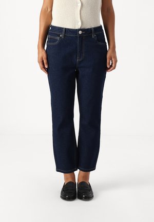 Tummansiniset farkut suoranlahkeisella muotoilulla, hienovaraisella kultasaumalla ja klassisella viiden taskun tyylillä. Yhdistetty mustiin loafer-kengiin.
