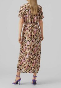 Maxi šaty s květinovým vzorem v odstínech růžové, béžové a hnědé. Krátké rukávy, páskový pas a volná látka. Spárováno s fialovými sandály na podpatku.